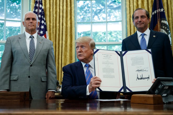 President Donald Trump, joined by joined by Vice President Mike Pence, left, and Secretary of Health and Human Services Alex Azar, right, holds up a $4.6 billion aid package to help the federal government cope with the surge of Central American immigrants at the U.S.-Mexico border, that he signed during a ceremony in the Oval Office of the White House in Washington, Monday, July 1, 2019. (AP Photo/Carolyn Kaster)
