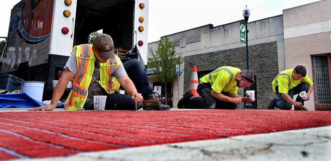 Todd Kriesen, left, Jay Fink and Paul Marino of Felix A. Marino Co., apply gray touch-up paint on a downtown Milford crosswalk Tuesday. Workers put down a base of gray paint and then sprayed red paint over stencils to give the illusion of brick. The touch-up paint is just for uneven portions of pavement not adequately covered by the stencils, according to Paul Marino. The company expected to finish five crosswalks in the downtown Milford area by Wednesday, just in time for Thursday's Fourth of July Parade. [Daily News and Wicked Local Staff Photo/Ken McGagh[