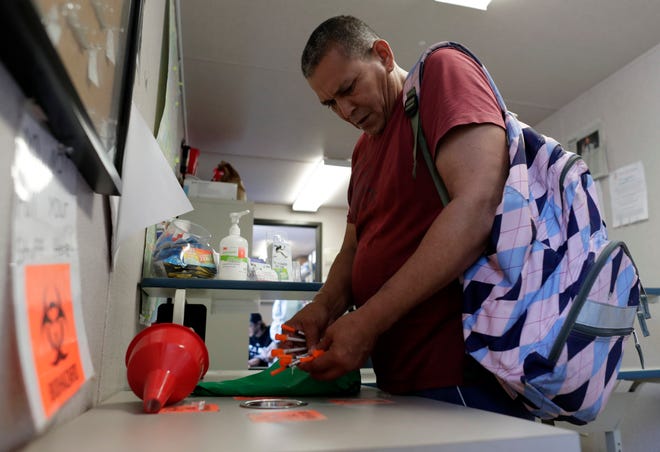 In this Monday, May 6, 2019 photo, Jose Garcia, an injection drug user, deposits used needles into a container at the IDEA exchange, in Miami. The University of Miami pilot program allows users to exchange used syringes for clean ones in order to avoid the transmission of HIV, Hepatitis C and other blood-borne diseases. Needle exchanges could eventually come to other parts of the state under a new law signed by Gov. Ron DeSantis. (AP Photo/Lynne Sladky)