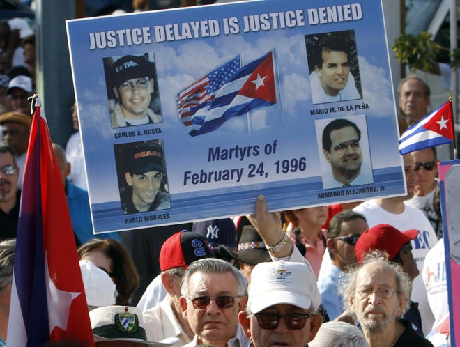 Mario de la Pena carries a poster with the photos of the four pilots shot down by Cuban MiGs, during a freedom for Cuba march in Miami in 2011. His son Mario de la Pena, top right, was among the pilots. [AP Photo/Alan Diaz, File]