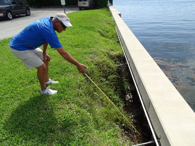 Tony Maxwell, a Hypoluxo Point resident, uses a tape measure to show the depth of an embankment south of Periwinkle Drive. [EMILY SULLIVAN/palmbeachpost.com]