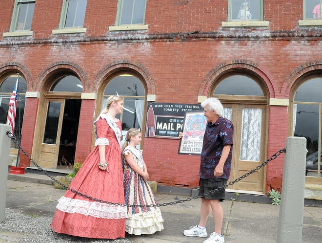 Bill Armstrong shows off a Ringling Bros and Barnum and Bailey Circus poster to 2018 Ohio Hills Folk Festival royalty Queen Olivia Neuhart and Princess Maggie Schnegg outside the Country Store Museum in Quaker City.