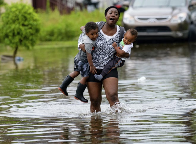 Terrian Jones reacts as she feels something moving in the water at her feet as she carries Drew and Chance Furlough to their mother on flooded Belfast Street in New Orleans on Wednesday. [Matthew Hinton/The Associated Press]