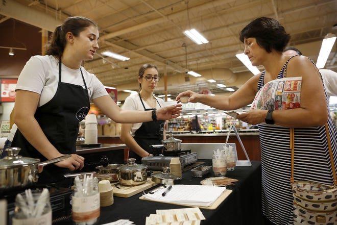 Amanda Pennings, left, the communications director at aha Pure Foods, hands Bonnie Corona, right, a sample cup of mushroom and vegetable soup during a tasting event at Lucky's Market, in Gainesville Fla., July 13, 2019. Aha Pure Foods, which produces their food products locally, will be competing in a startup competition later this month. [Brad McClenny/The Gainesville Sun]