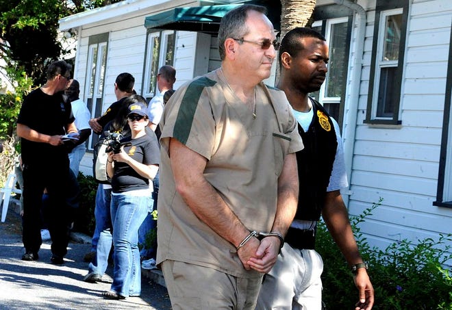 In this Feb. 2011 photo a DEA agent escorts Zvi Harry Perper to an awaiting police car after his Delray Pain Management clinic was raided by agents in Delray Beach, Fla.