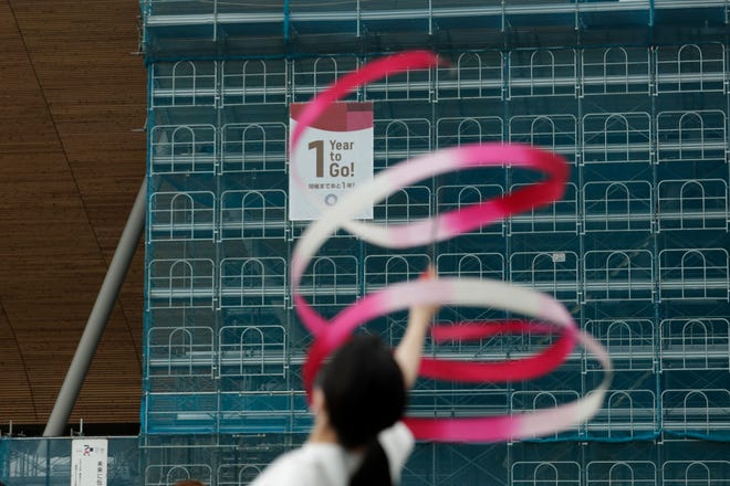 Former Japanese Olympic gymnast Kotono Tanaka performs as a "1-Year to Go" banner hangs outside the Ariake Gymnastics Center on Monday in Tokyo. Despite scandals, rising costs and doubts about the economic payoff, the Tokyo Olympics will be a must-see event — if you can find a ticket or a hotel room — when they open in a year. Tokyo was supposed to be a "safe pair of hands" after Rio de Janeiro's corruption and near-meltdown three years ago. [Jae C. Hong/The Associated Press]