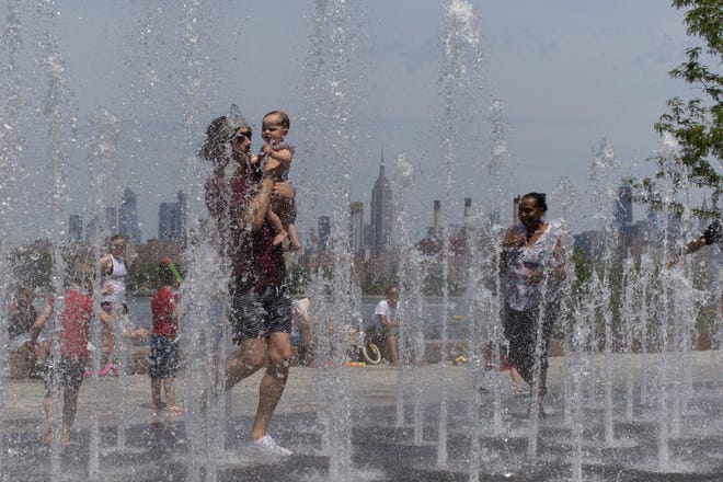 People enjoy the day playing in a water fountain as the Empire State Building is seen from Williamsburg section of Brooklyn on Saturday, July 20, 2019 in New York. Americans from Texas to Maine sweated out a steamy Saturday as a heat wave spurred cancelations of events from festivals to horse races and the nationþÄôs biggest city ordered steps to save power to stave off potential problems.  (AP Photo/Eduardo Munoz Alvarez)