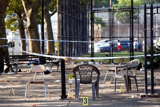 Yellow evidence markers are placed next to chairs at a playground in the Brownsville neighborhood in the Brooklyn borough of New York, Sunday, July 28, 2019. Police said, one man was killed and at least 11 others were injured in a shooting late Saturday night at the park. (AP Photo/Mark Lennihan)
