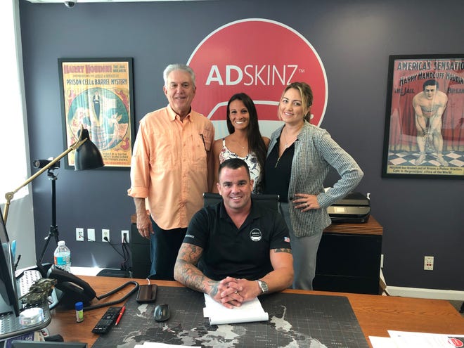 Jason Mariner, CEO of Adskinz with his wife Charlene (back row, right) first operated the company out of their garage before moving to their office space in Palm Beach Gardens. [Adriana Delgado/The Palm Beach Post]