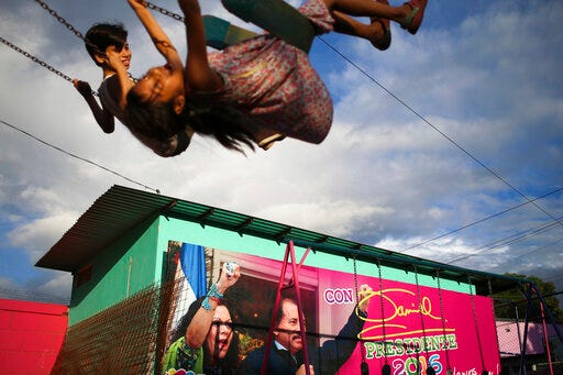 FILE - In this Nov. 4, 2016 file photo, children swing in a park next to an election billboard promoting Nicaragua's President Daniel Ortega and running mate, his wife Rosario Murillo in Managua, Nicaragua. Nicaraguan opposition leaders returned to the negotiating table Wednesday, July 31, 2019, at a business center where talks on resolving the country's political crisis stalled months ago, but there was nobody there to talk to. The opposition wants Ortega, 73, to negotiate electoral reform and early elections. (AP Photo/Esteban Felix, File)