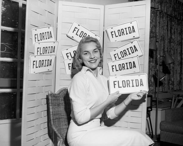 Florida State University junior Jean Hayden promoting "Florida" tags in Tallahassee, Florida photographed on January 24, 1957. Accompanying note: "Jean Hayden, Florida State University junior from Jacksonville, is helping the Tallahassee Junior Chamber of Commerce to boost sale of 'Florida' tags this year. The tags are on sale for 50 cents at the tax collector's office in the court house where regular license tags are being sold, at the U.S. Royal Tire Service on north Monroe St., at the State Motor Vehicle tag agency and at General Travel Service on Call St." (State Archives of Florida)