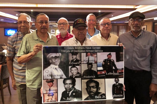 From left, Eddie Davis and his brothers Julius, Octavious, Lebronze, Frederick, Arguster and Nathaniel pose for a photo behind a family picture during a reunion at a hotel-casino on Friday, July 12, 2019, in Tunica, Miss. Eleven in all, their combined 158 years of service to the U.S. military make them brothers in arms as well as brothers raised on a family farm in rural Alabama. [AP Photo/Adrian Sainz]