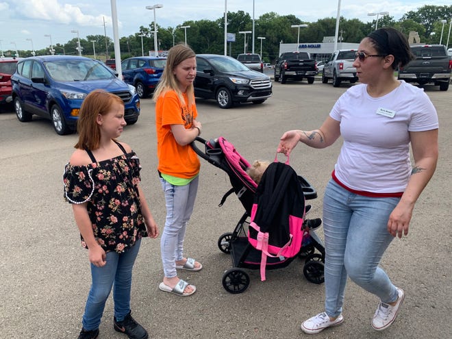 From left, K-Lee Woosley, a fifth-grader at Lowman Hill Elementary School, and her mother, Emily Adams, look on as Kayla Morgan, of Laird Noller Ford, brings a backpack for K-Lee during an event Saturday morning at Laird Noller Ford, 2245 S.W. Topeka Blvd. The dealership provided 215 backpacks filled with school supplies to students who pre-registered from Lowman Hill and Quincy Elementary Schools. [Phil Anderson/The Capital-Journal]