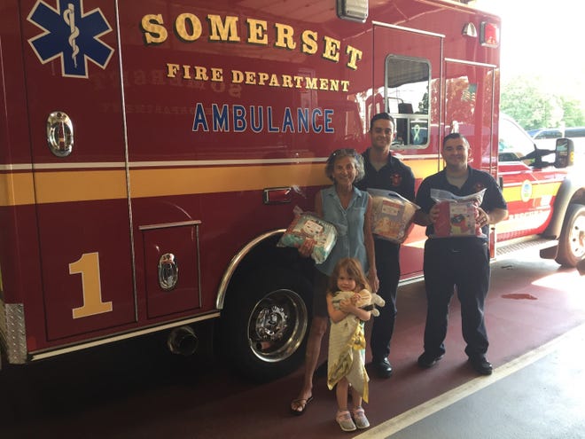 Katheen Sampson, with granddaughter Brooklyn, distributes Buddy Bags to Somerset Fire Department firefighters Justin Raulino and Jordan DeMelo. [Courtesy Photo]