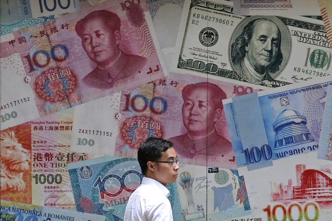 FILE - In this June 10, 2019, file photo, a man walks past a money exchange shop decorated with different banknotes at Central, a business district of Hong Kong. China's yuan fell below the politically sensitive level of seven to the U.S. dollar on Monday, Aug. 5, 2019, possibly adding to trade tension with Washington. The currency weakened to 7.0177 in early trading following U.S. President Donald Trump's threat last week of tariff hikes on additional Chinese imports in a fight over Beijing's trade surplus and technology policies. (AP Photo/Kin Cheung, File)