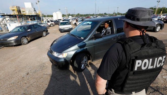 A federal agent directs a vehicle to approach as they begin to clean out the parking lot at a Koch Foods Inc., plant in Morton, Miss., on Wednesday. The agent was one of many who participated in the early morning raid that was part of a large-scale operation targeting owners as well as undocumented employees.