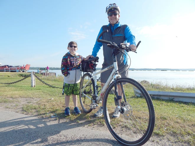 Eric Eckard got some assistance from seven-year-old Wyatt Stokley, part of his support team, as he prepared to leave Rotary Park Wednesday morning. Eckard will be covering approximately 700 miles over the next two weeks in a solo bike trip — Ride for Neal — to raise money and awareness after losing his older brother to cancer in November. (Scott Brand/The Sault News)