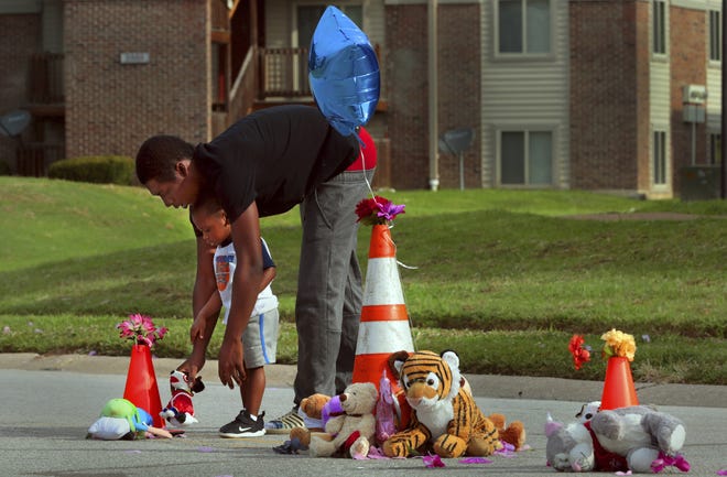 Canfield Green Apartments resident Marcus Hill helps his son Messiah Hill, 2, place a stuffed animal at a newly rebuilt memorial to Michael Brown, Jr. on Thursday in Ferguson. The site is where Brown was shot and killed by a Ferguson police officer on Aug. 9, 2014. "We see his father all the time," said Hill of Michael Brown, Sr. "I've got my own son, and I know it's hard for him this time of year." [Robert Cohen/St. Louis Post-Dispatch via AP]