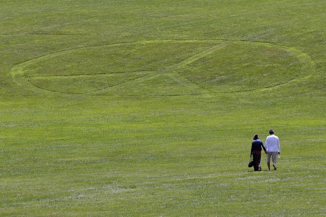 Carol Laura, left, and George Acquaire walk barefoot to a peace sign mowed in the grass at the site of the 1969 Woodstock Music and Arts Fair on July 24 in Bethel. Woodstock will be celebrated on its 50th anniversary, but it won't be your hippie uncle's trample-the-fences concert. While plans for a big Woodstock 50 festival collapsed after a run of calamities, the bucolic upstate New York site of the 1969 show is hosting a long weekend of events featuring separate shows by festival veterans like Carlos Santana and John Fogerty. [SETH WENIG/ASSOCIATED PRESS]