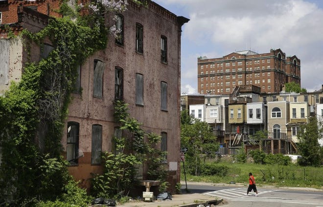 FILE PHOTO: In this May 9, 2015, file photo, a man walks past a blighted building in the Penn-North neighborhood of Baltimore, with a residential tower in the Reservoir Hill neighborhood in the background at top right.