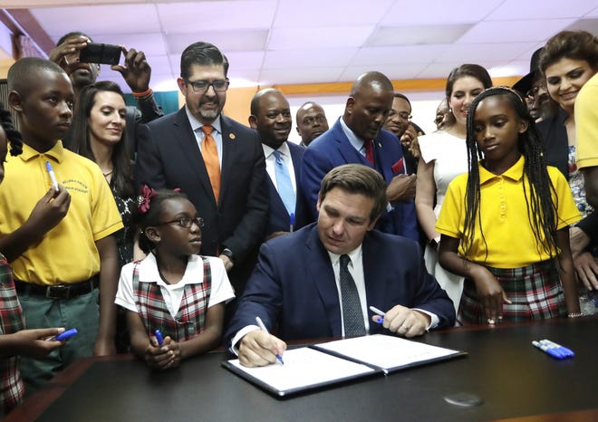 Florida Gov. Ron DeSantis, center, signs a bill during a ceremony at the William J. Kirlew Junior Academy May 9 in Miami Gardens. The bill creates a new voucher program for thousands of students to attend private and religious schools using taxpayer dollars traditionally spent on public schools. [AP Photo/Lynne Sladky/ File]
