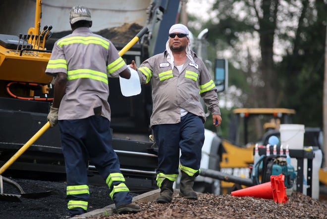 Hector Alexander offers Royyell Pearce a jug of water at a paving job in Shelby on Tuesday. [Brittany Randolph/The Star]