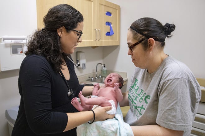 In this Aug. 13, 2019, photo, Dr. Jasmine Saavedra, left, a pediatrician at Esperanza Health Centers in Chicago, hands newborn Alondra Marquez to her mother, Esthela Nunez, right, after examination. Doctors and public health experts warn of poor health outcomes and rising costs they say will come from sweeping changes that would deny green cards to many immigrants who use Medicaid, as well as food stamps and other forms of public assistance. (AP Photo/Amr Alfiky)