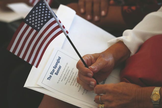 In this Aug. 16, 2019, file photo a citizen candidate holds an American flag and the words to The Star-Spangled Banner before the start of a naturalization ceremony at the U.S. Citizenship and Immigration Services Miami field office in Miami.