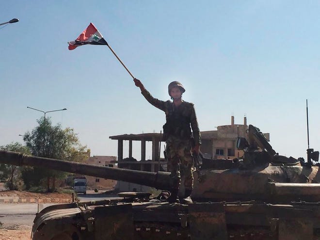 A Syrian soldier stands on a tank waving a national flag in the northwestern town of Khan Sheikhoun, Syria, on Saturday. The town was captured by Syrian troops last week after a monthslong offensive. (AP Photo/Albert Aji)