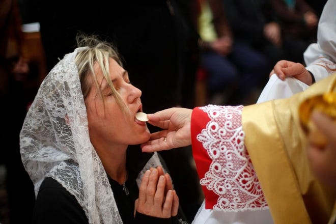 A Catholic woman receives Communion, or the Eucharist, which Catholic doctrine teaches is the body of Christ after being consecrated by a priest during mass.