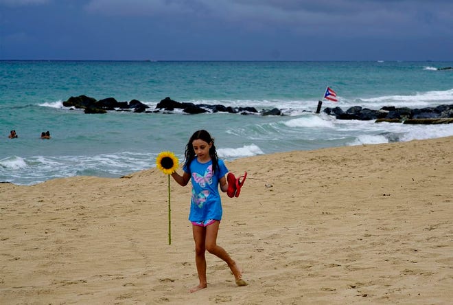 A girl walks on a sandy beach holding a sunflower and her flip flops after the passing of Tropical Storm Dorian, in the Condado district of San Juan, Puerto Rico, Wednesday, Aug. 28, 2019. The Hurricane Center said the storm could grow into a dangerous Category 3 storm as it pushes northwest in the general direction of Florida.