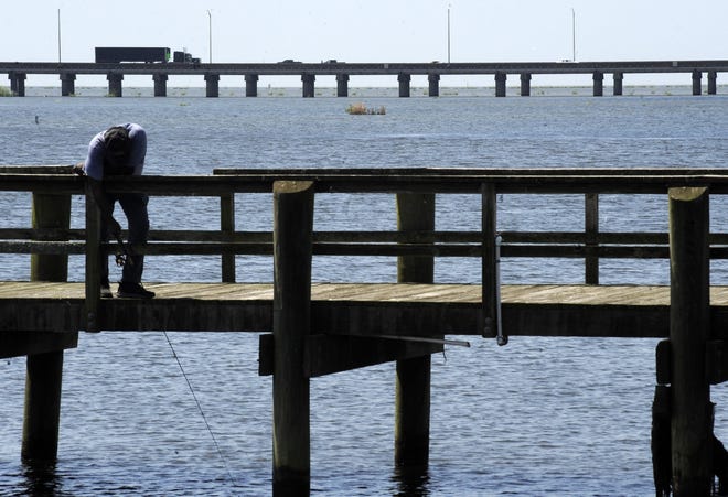 A man fishes on a pier as traffic on Interstate 10 crosses Mobile Bay at Spanish Fort on Wednesday, Aug. 28, 2019. Officials in Baldwin County took a decisive stand against a plan to use tolls to pay for a replacement bridge and roadway, prompting Alabama Gov. Kay Ivey to say the project was now dead. [AP Photo/Jay Reeves]