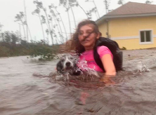Julia Aylen wades through waist deep water carrying her pet dog as she is rescued from her flooded home during Hurricane Dorian in Freeport, Bahamas, Tuesday, Sept. 3, 2019. Practically parking over the Bahamas for a day and a half, Dorian pounded away at the islands Tuesday in a watery onslaught that devastated thousands of homes, trapped people in attics and crippled hospitals. (AP Photo/Tim Aylen)