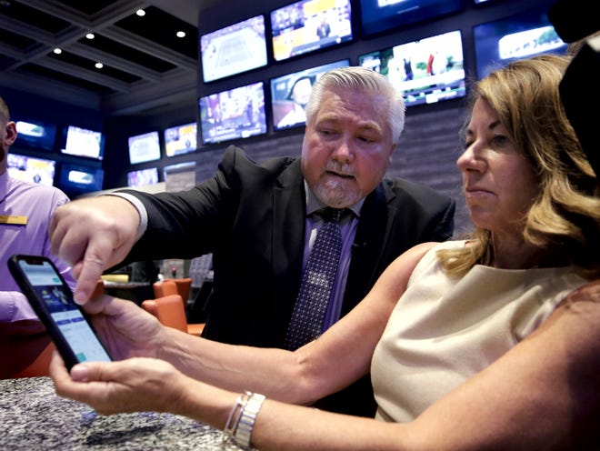 Joe Franklin, Twin River Casino's regional executive director of cage operations, takes Twin River spokeswoman Patti Doyle through the installation and activatation of the state's new SportsBook App on her phone in the Twin River SportsBook Bar & Grill on Wednesday. [The Providence Journal / Kris Craig]
