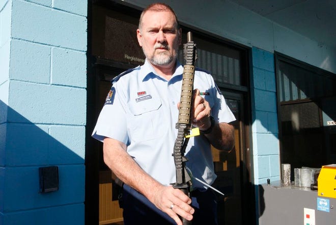 In this Aug. 31, 2019, photo. Police Senior Sgt. Braydon Lenihan poses holding a banned gun that has been bent by a hydraulic machine outside a temporary gun collection venue in Porirua, near Wellington, New Zealand. New Zealand is six weeks into an ambitious program to buy tens of thousands of guns from owners across the country. (AP photo/Nick Perry)