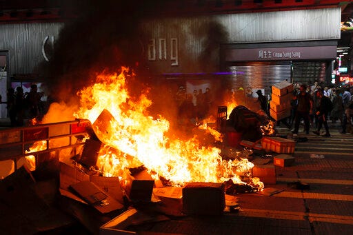 Protesters stand near burning items during a protest during a protest in Mong Kok, Hong Kong on Friday, Sept. 6, 2019. The ratings agency Fitch on Friday cut Hong Kong's credit rating and warned that conflict with anti-government protesters was hurting the image of its business climate. (AP Photo/Kin Cheung)