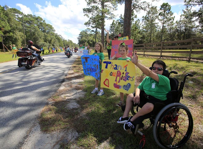 Ashton Giddens, right, Piper Temple and Teagan Temple wave to bikers as they head into Camp Boggy Creek during the 19th annual Bruce Rossmeyer Ride for Children to Camp Boggy Creek in Eustis. [Gatehouse Florida File]