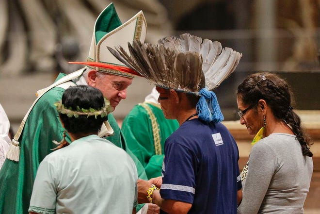 Indigenous peoples, some with their faces painted and wearing feathered headdresses, stand by Pope Francis as he celebrates an opening Mass for the Amazon synod, in St. Peter's Basilica, at the Vatican on Sunday. Pope Francis is opening a divisive meeting on preserving the Amazon and ministering to its indigenous peoples, as he fends off attacks from conservatives who are opposed to his ecological agenda. [Andrew Medichini/The Associated Press]