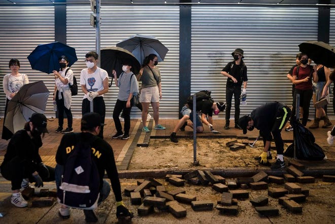 People watch as protesters remove bricks from the sidewalk to make a road block in Hong Kong, Hong Kong, Monday, Oct. 7, 2019. Tens of thousands of masked protesters marched defiantly in the city center Sunday, but the peaceful rallies quickly degenerated into chaos at several locations as hard-liners again lobbed gasoline bombs, started fires and trashed subway stations and China-linked banks and shops. (AP Photo/Felipe Dana)