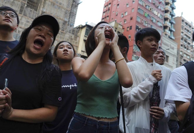 Pedestrian shout slogan during a protest in Hong Kong on Saturday. Protesters marching peacefully hit the rain-slickened streets of Hong Kong again in multiple locations on Saturday, defying police warnings that they were gathering illegally. [VINCENT YU/THE ASSOCIATED PRESS]