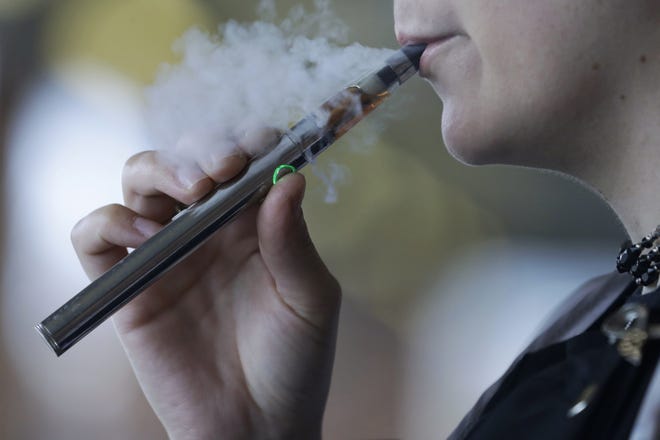 A woman exhales Oct. 4 while using an e-cigarette in Mayfield Heights. An Ohio law banning tobacco and nicotine sales to anyone under age 21 goes into effect Thursday. (AP Photo/Tony Dejak, File)