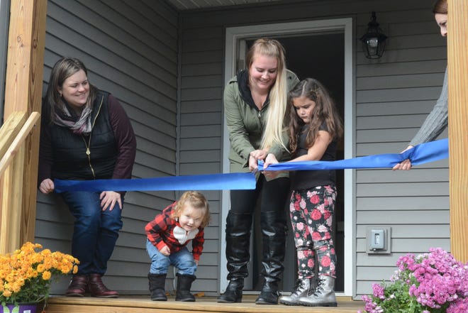 Hannah Lulham, center, cuts the ribbon at her new home in Adrian with her children by her side and Carrie Hartley of Lenawee County Habitat for Humanity holding one end of the ribbon, left, during the dedication Sunday. [Telegram photo by Hannah Warner]