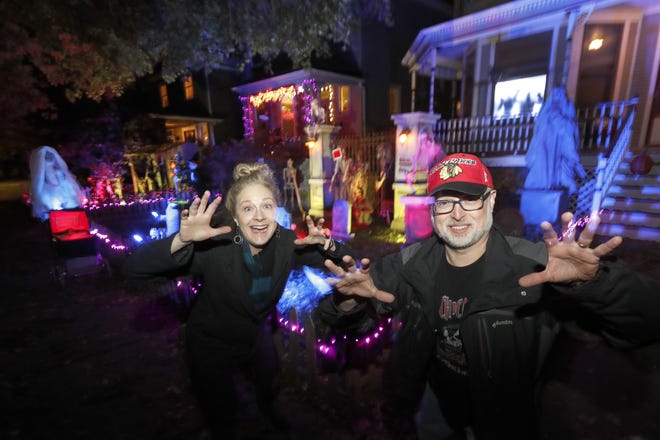 In this Tuesday, Oct. 29, 2019 photo, neighbors Beth LeFauve, left, and Nelson Gonzalez pose for a portrait outside their two Bernard Street homes and the Halloween decorations spanning both properties in Chicago. The good news for kids trick-or-treating this Halloween: They're much more likely to encounter candy than a healthier alternative. Americans this year have a wide variety of plans to celebrate the spooky holiday, from carving pumpkins to watching scary movies. Those are some of the findings of a poll conducted ahead of Halloween by The Associated Press-NORC Center for Public Affairs Research. (AP Photo/Charles Rex Arbogast)