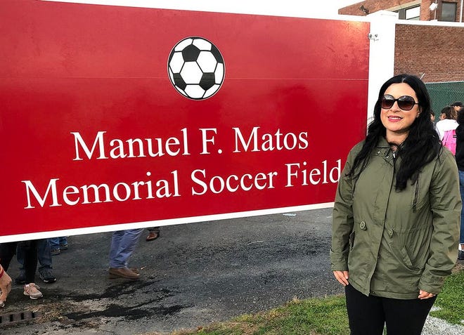 Bethany Matos Austin, filha de Manny Matos, junto ao placard a assinalar o campo de futebol do Liceu de New Bedford baptizado com o nome do seu pai.