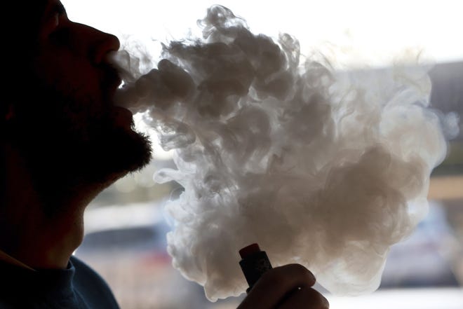 In this Jan. 18, 2019 file photo, a man exhales a puff of smoke from a vape pipe at a shop in Richmond, Va. Ohio State University researchers who reviewed studies exploring the effect of e-cigarettes on the heart are advising against using the devices. [Steve Helber/AP]
