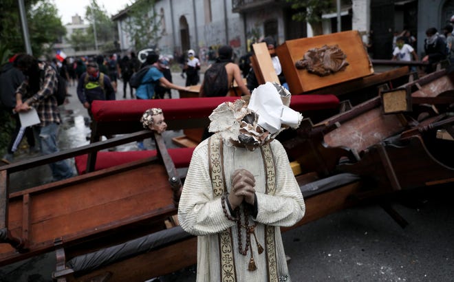 A damaged statue taken from a church forms part of barricade created by antigovernment protesters, in Santiago, Chile, on Friday. Chile's president on Thursday announced measures to increase security and toughen sanctions for vandalism following three weeks of protests that have left at least 20 dead. [ESTEBAN FELIX/THE ASSOCIATED PRESS]