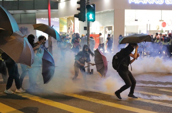 Protesters use umbrellas to protect themselves as they face police teargas in Hong Kong on Sunday. Protesters smashed windows in a subway station and a shopping mall Sunday and police made arrests in areas across Hong Kong amid anger over a demonstrator's death and the arrest of pro-democracy lawmakers.Hong Kong is in the sixth month of protests that began in June over a proposed extradition law and have expanded to include demands for greater democracy and other grievances. [KIN CHEUNG/THE ASSOCIATED PRESS]