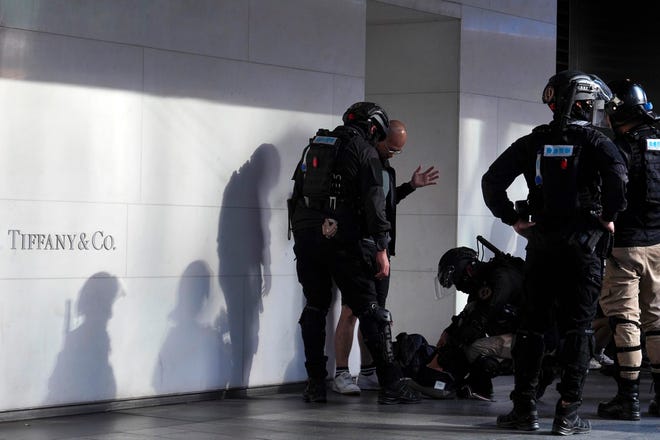 Riot police search a man's belonging during a rally in Central, Hong Kong, on Tuesday. Police fired tear gas at protesters who littered streets with bricks and disrupted morning commutes and lunch breaks Tuesday after an especially violent day in Hong Kong's five months of anti-government demonstrations. [VINCENT YU/THE ASSOCIATED PRESS]