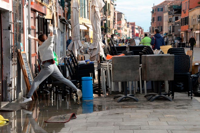 A woman jumps over a puddle during cleaning following a flooding in Venice, Italy, Thursday, Nov. 14, 2019. The worst flooding in Venice in more than 50 years has prompted calls to better protect the historic city from rising sea levels as officials calculated hundreds of millions of euros in damage. The water reached 1.87 meters above sea level Tuesday, the second-highest level ever recorded in the city. (Andrea Merola/ANSA via AP)
