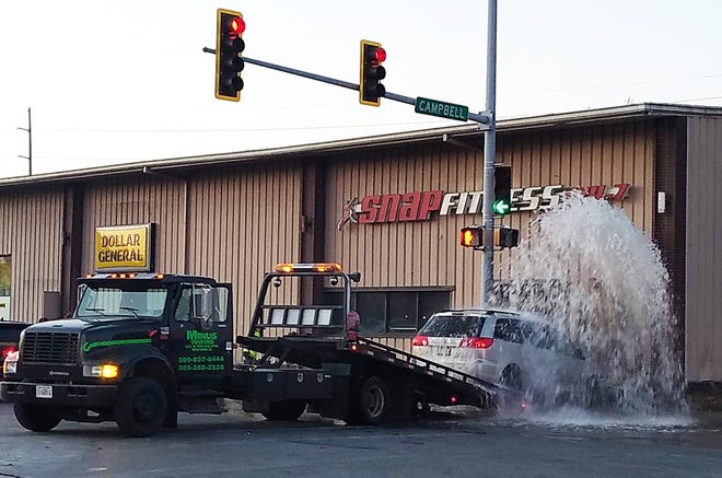 A jet of water shoots from the opening at SNAP Fitness made by a silver minivan as it is winched onto a tow vehicle. The cause of the collision and whether there were any inuries was not known by press time. [MICHELLE LANGHOUT/THE VOICE]